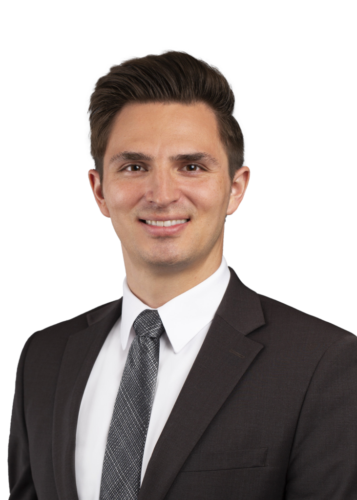 Portrait of a smiling man in a dark suit, white shirt, and patterned tie, against a black backdrop (business headshot).